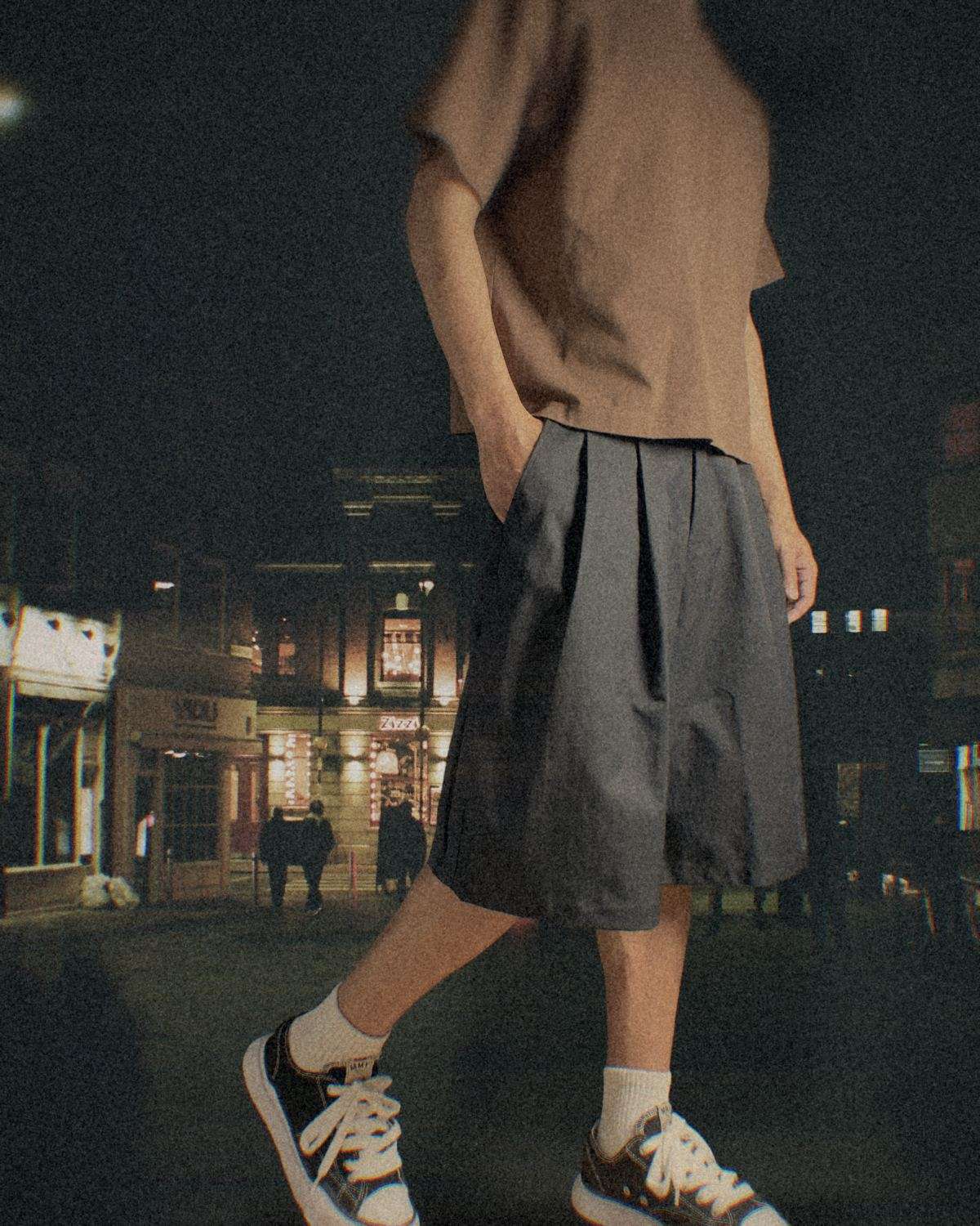 Someone walking down a night street in black pleated wide shorts