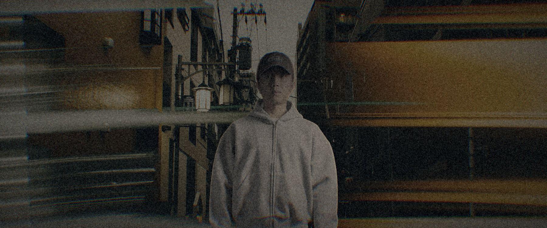 穿著麻灰連帽外套站在夜晚街頭,背後是車燈的光軌